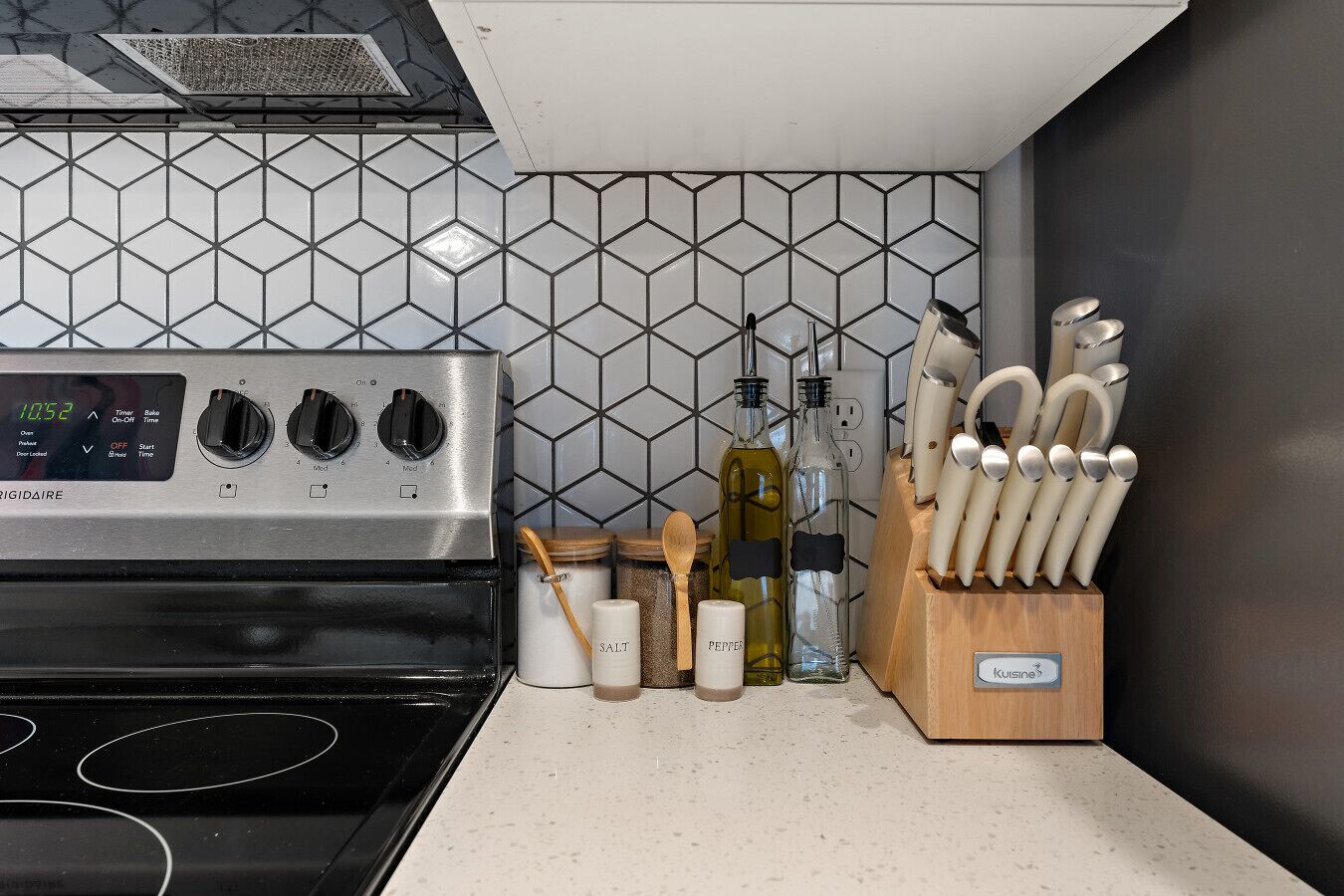 Een keuken met een roestvrijstalen fornuis, een backsplash van honingraatmozaïek en een messenblok op het aanrecht.