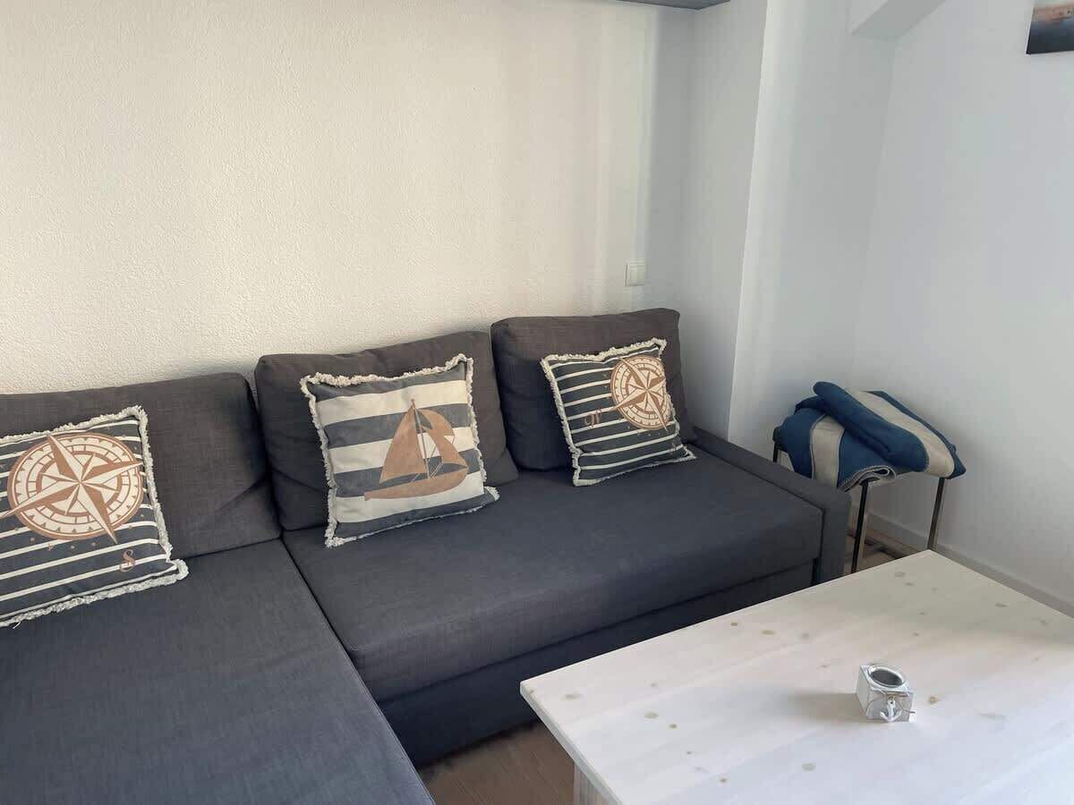 Una sala de estar moderna con un sofá gris, almohadones a rayas y una pequeña mesa blanca.