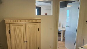 Une chambre à coucher comprenant un lit, une armoire, une petite table et une porte donnant sur une autre pièce.