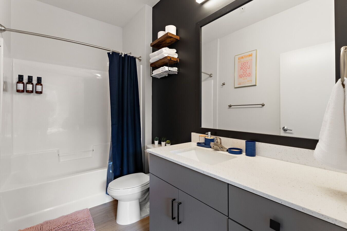 Un baño moderno con una bañera blanca, una cortina de ducha, un inodoro, un tocador con espejo y un estante con artículos de tocador.
