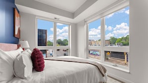 Ein Schlafzimmer mit einem großen Bett, Blick auf die Stadt durch große Fenster und einem modernen Design.