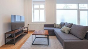 A modern living room with a sofa, a coffee table, a TV on a stand, and a window providing natural light. - Berlinkiez (Berlin)