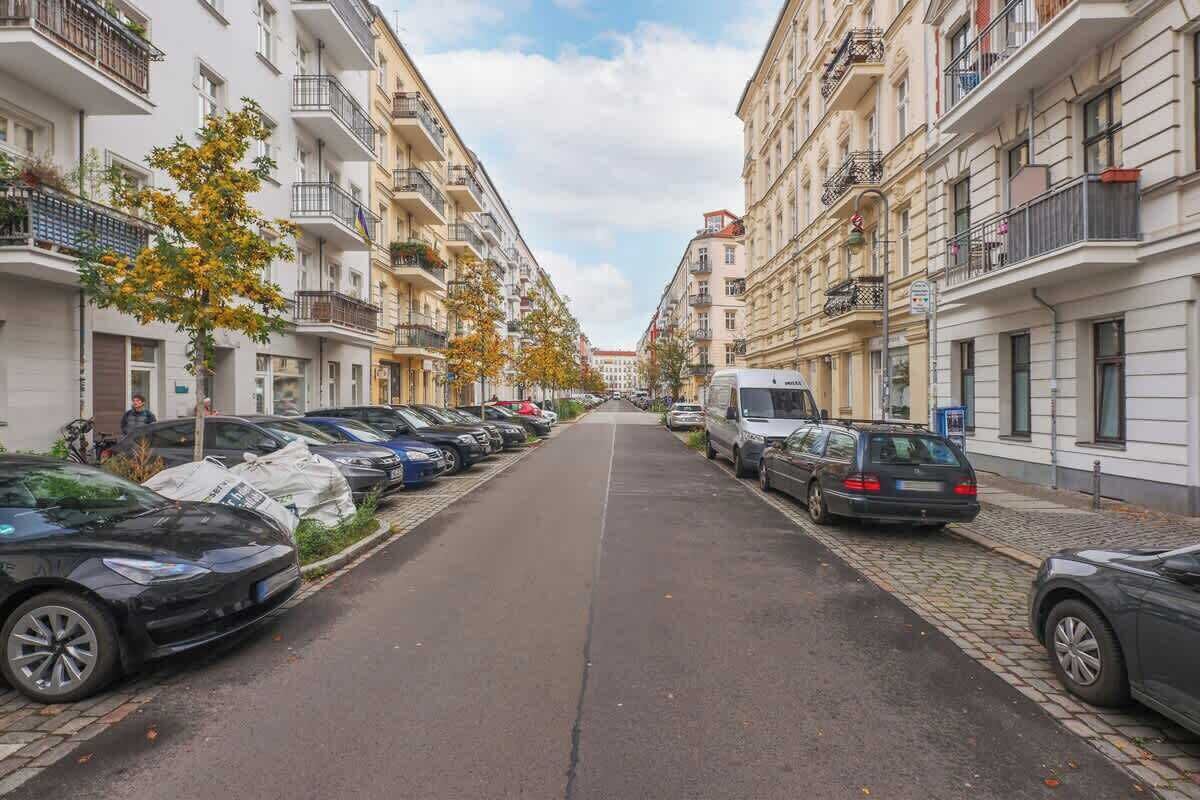 Eine Straße gesäumt von mehrstöckigen Wohnhäusern, parkenden Autos und einem klaren Himmel.