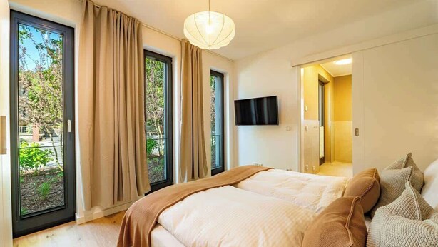 Ein Schlafzimmer mit einem großen Bett, einem an der Wand befestigten Fernseher und einer Schiebetür, die auf einen Balkon führt.