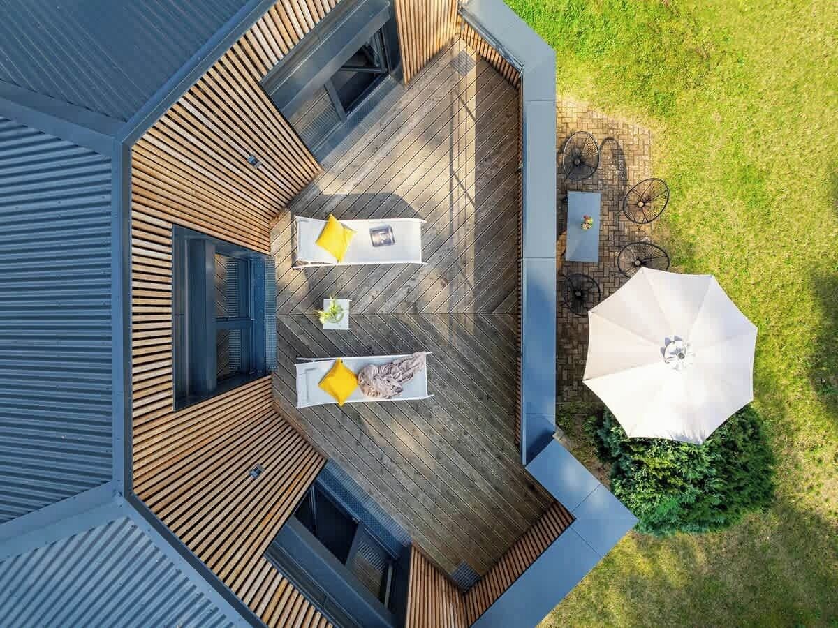 An aerial view of a modern house with a deck, two outdoor seating areas with yellow cushions, and a large umbrella.