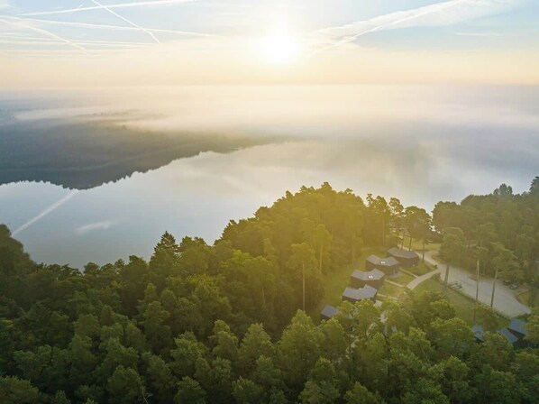 A serene lakeside view with a cluster of houses surrounded by dense forest. - Haus 1 - ELF AM SEE (Templin)