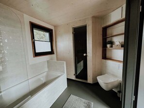 A bathroom with a bathtub, a toilet, and a shower area. - Haus 1 - ELF AM SEE (Templin)