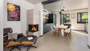 A modern living room with a fireplace, a dining area, and a kitchen. - Haus 1 - ELF AM SEE (Templin)