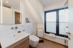 Een moderne badkamer met een groot raam, een wastafel met spiegel en een toilet.