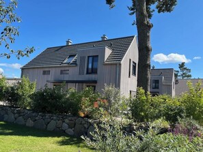 Een tweelaags huis met een stenen muur, een schuin dak en een tuin met verschillende planten.