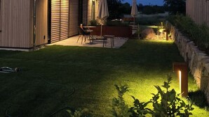 A modern house with a well-lit patio, outdoor furniture, and a stone retaining wall. - Holiday Home SandDorn 1 (Pruchten)