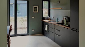 A modern kitchen with dark cabinets, a wooden countertop, and a view through the sliding glass door. - Elf am See - House 7 (Templin)
