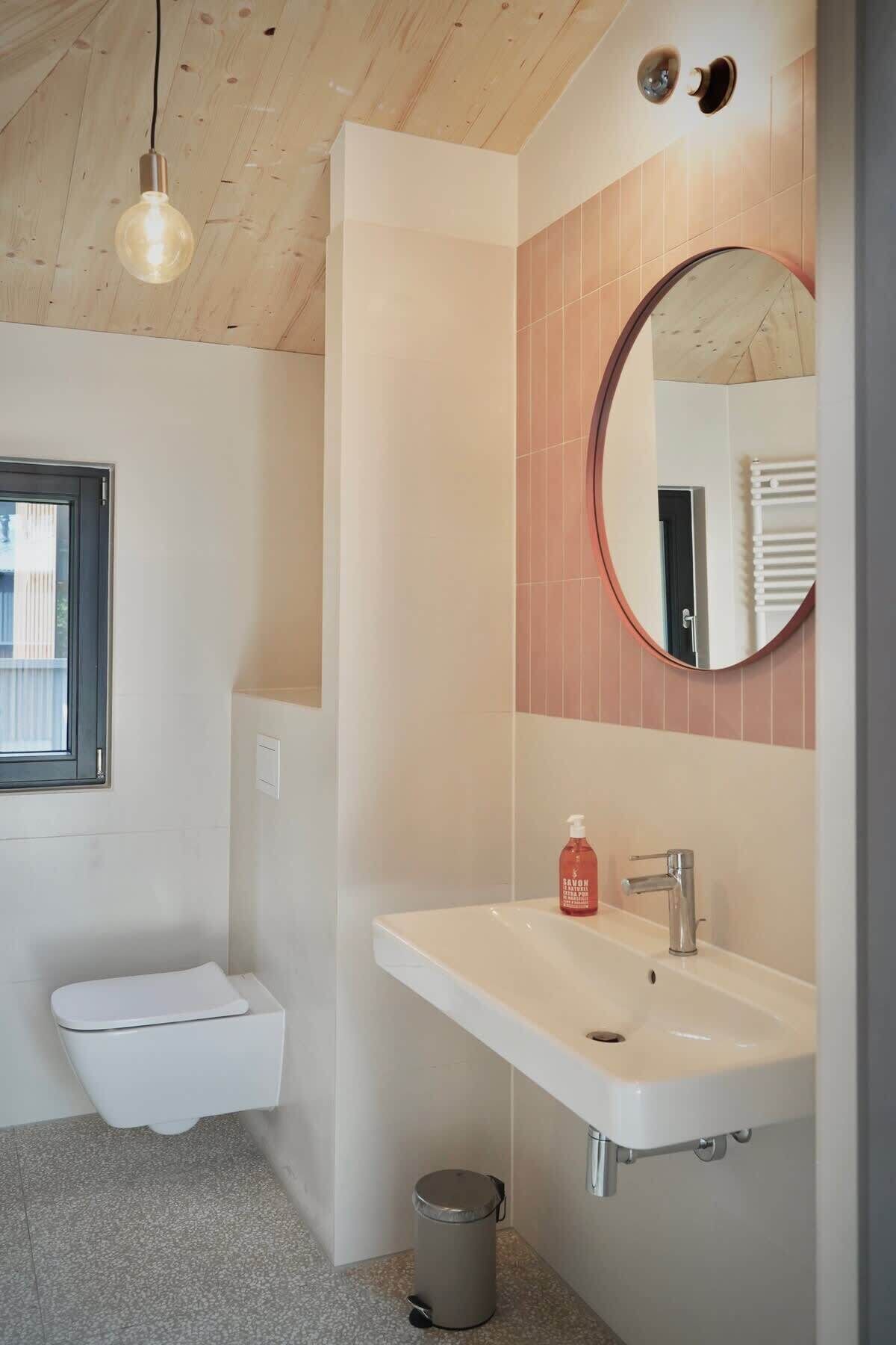 Une salle de bain moderne avec un lavabo blanc, un miroir rond et un luminaire suspendu.