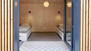 A small, cozy room with wooden walls and a tiled floor. There are two beds with white bedding and two wall-mounted lamps. - Elf am See - House 7 (Templin)
