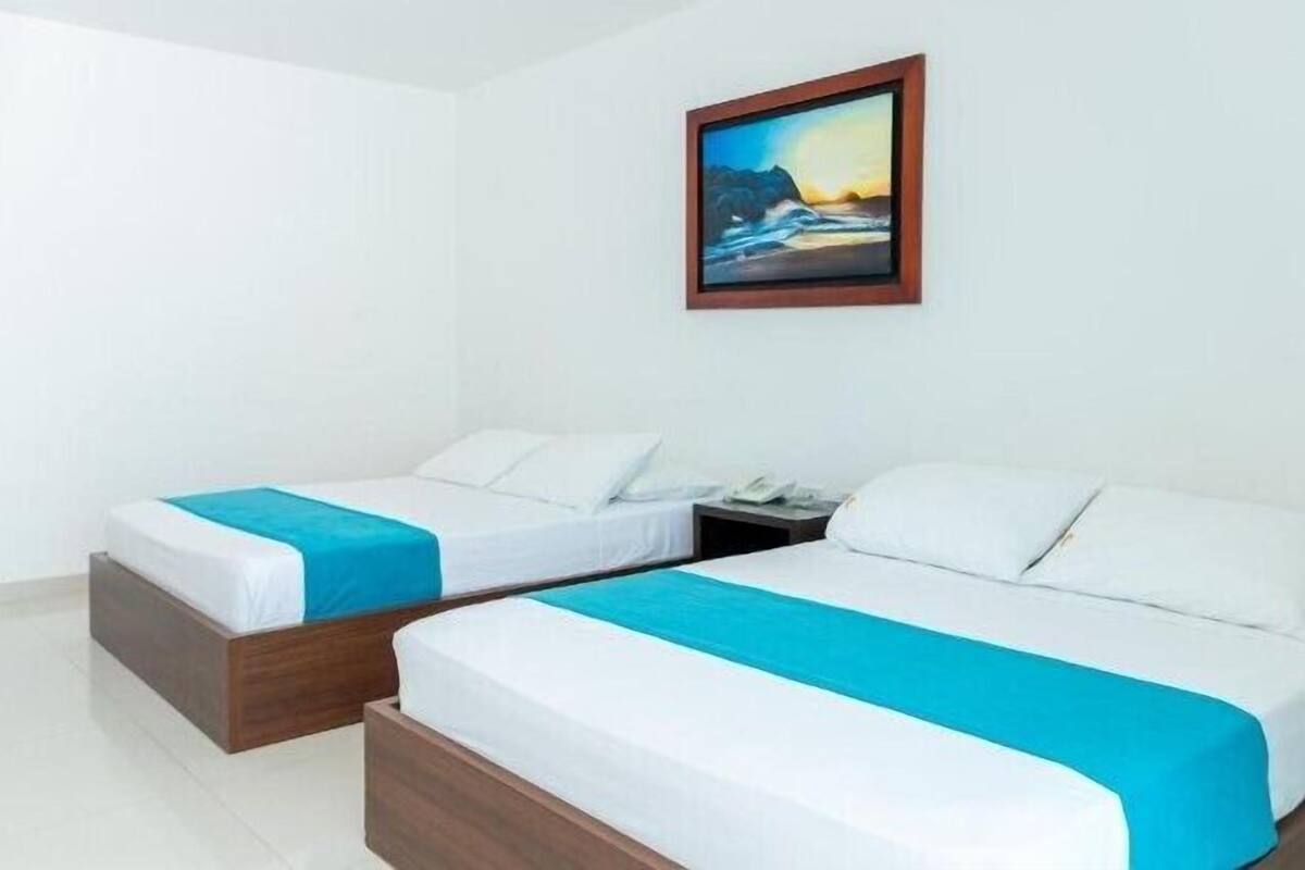 A hotel room with two single beds, white bedding, and a painting of a coastal scene.