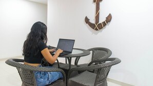 Una persona usando una computadora portátil en una mesa redonda con sillas de mimbre, en una habitación con pared blanca y un adorno de ancla de madera.