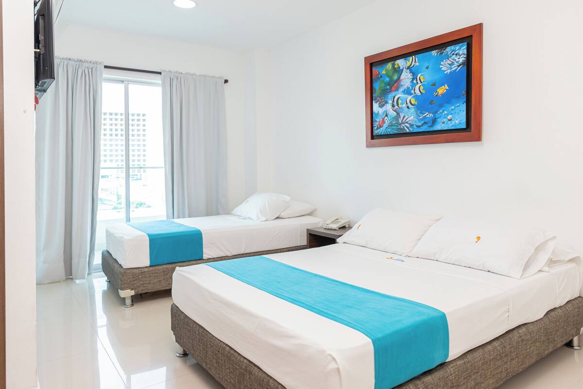 A hotel room with two beds, a painting of fish on the wall, and a window with curtains.