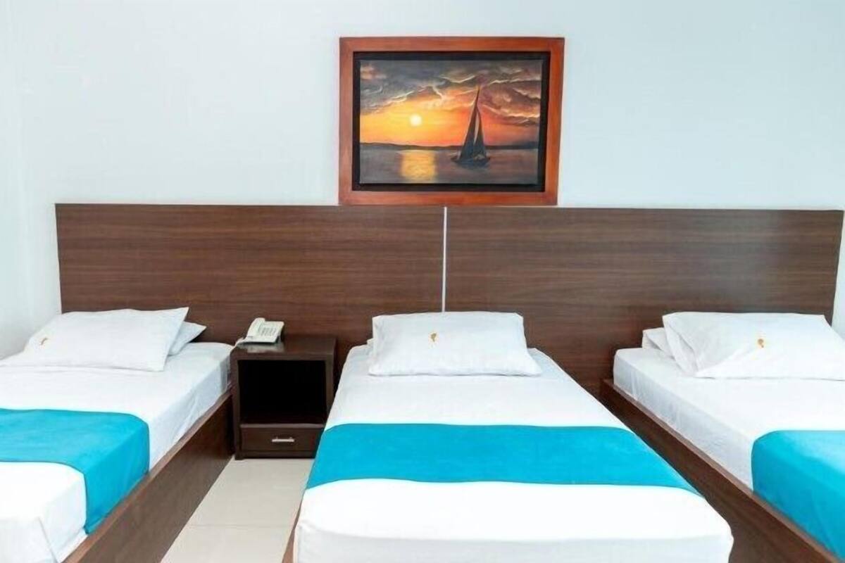 A hotel room with two beds, a nightstand, and a painting of a sunset over the ocean.