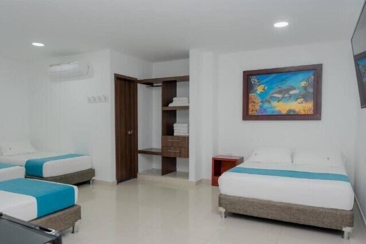 A hotel room with two beds, a wooden wardrobe, a painting, and a small table.