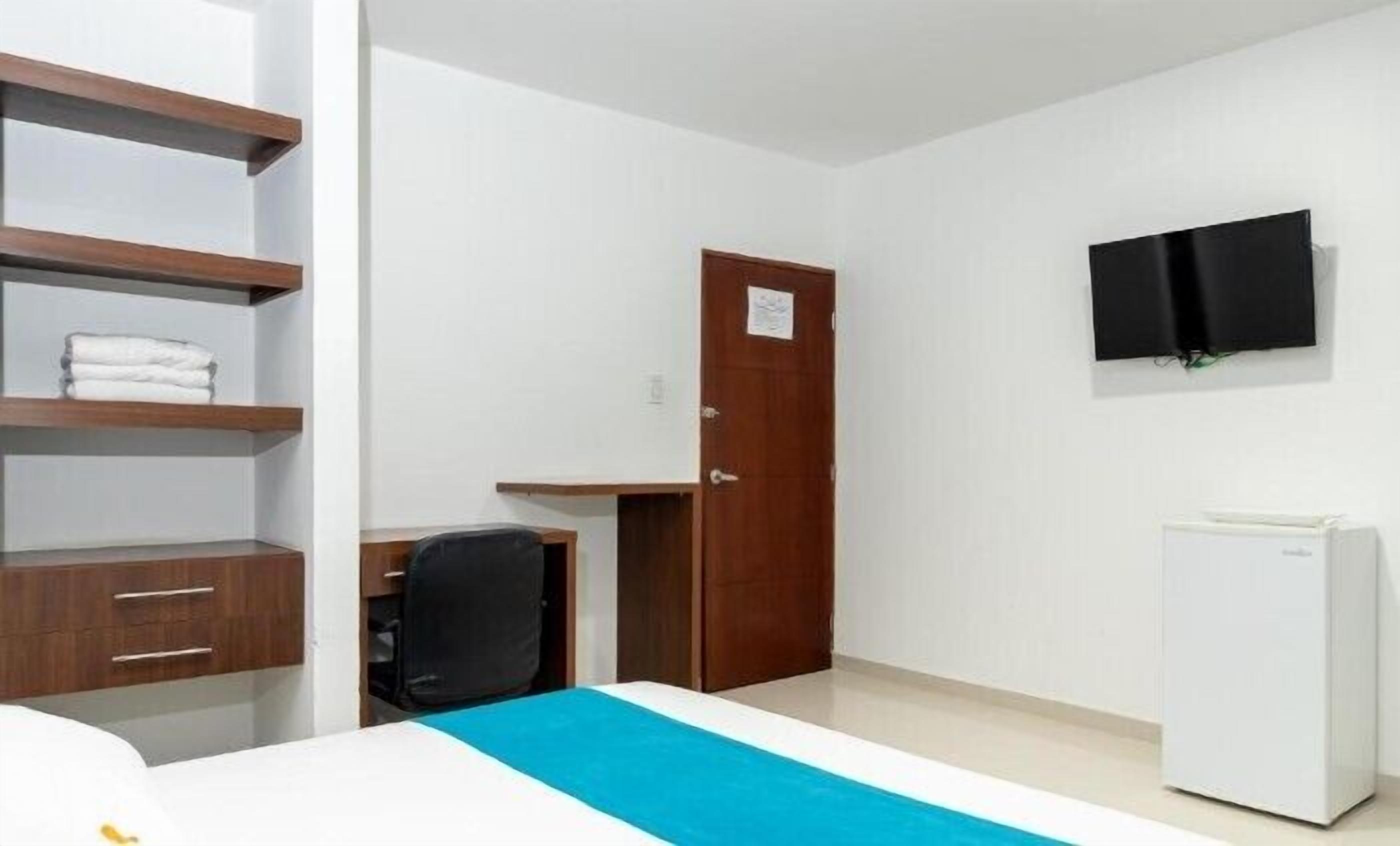 Een hotelkamer met een bed, bureau, stoel, televisie en een koelkast.