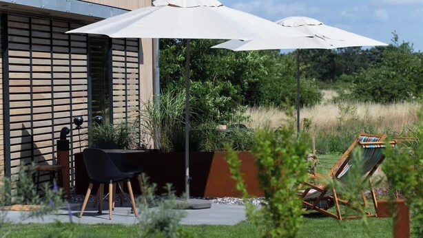 A modern house with a patio area featuring a dining table, chairs, and a large umbrella. - Holiday Home SandDorn 2 (Pruchten)