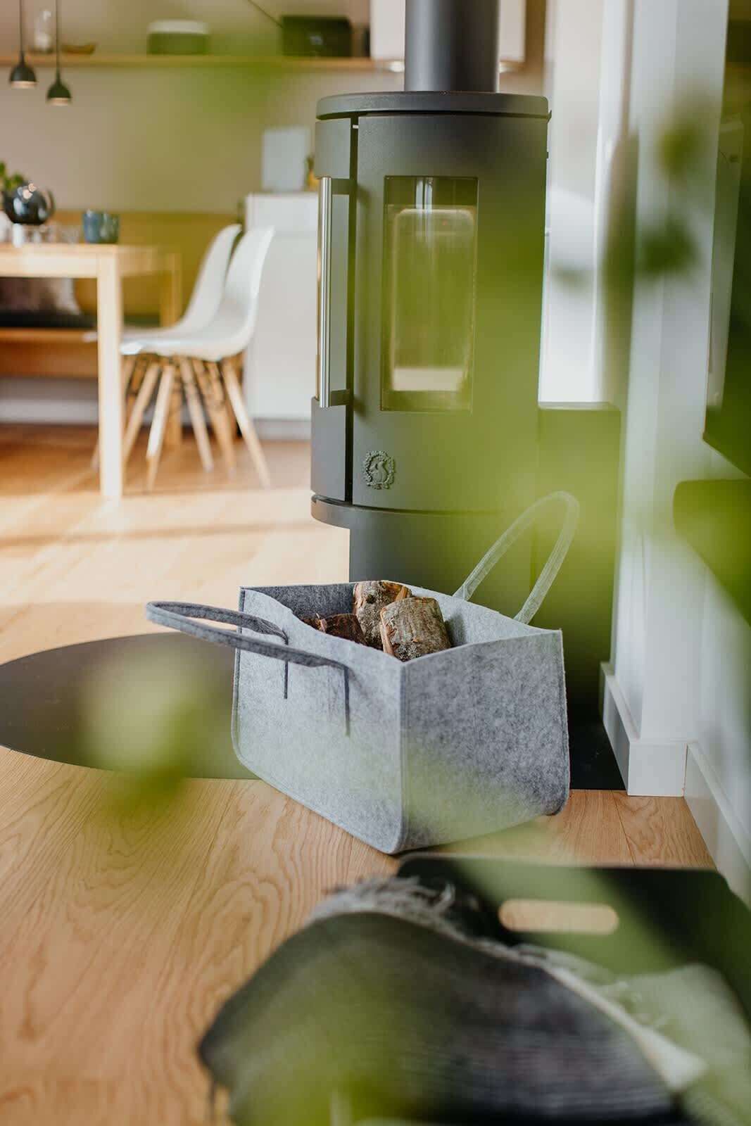 Una cucina moderna con stufa a legna, un contenitore portaoggetti grigio e un'area pranzo con tavolo e sedie in legno.