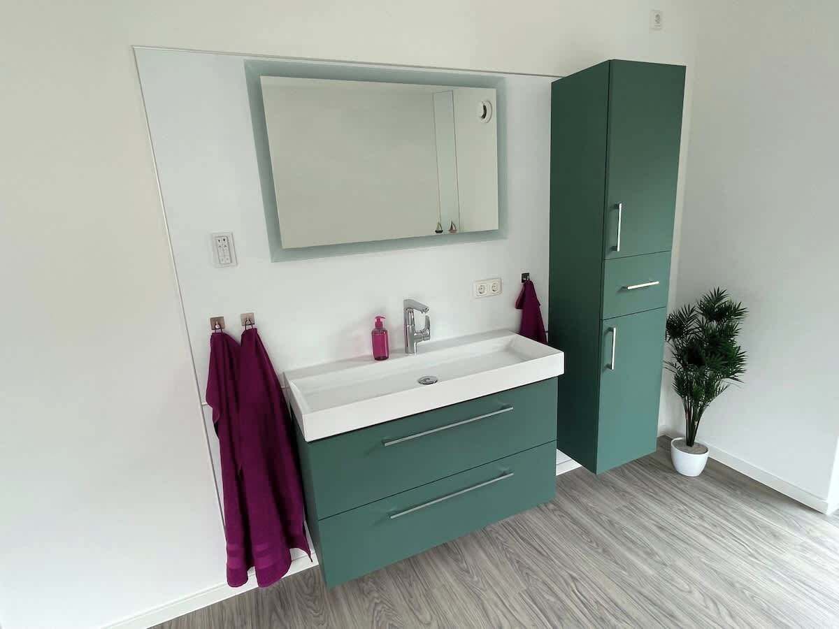 A bathroom with a white sink, green cabinets, and a mirror above the sink.