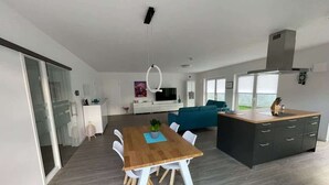 Una cocina moderna con una mesa de comedor de madera, sillas blancas y una isla oscura con un fregadero.