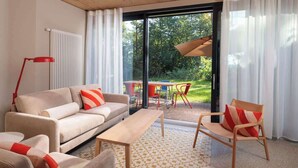 En moderne stue med sofa, lænestol og sofabord. Der er et spisebord med stole uden for en glasdør.
