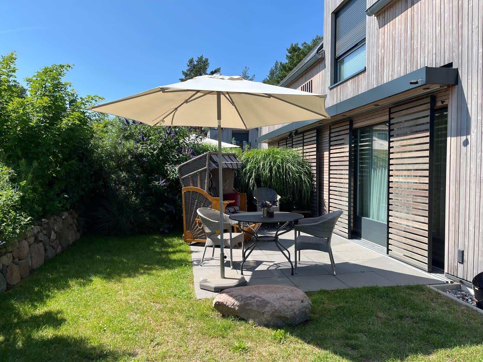 En udendørs terrasse med et bord, stole og en stor parasol, samt en stenvæg.