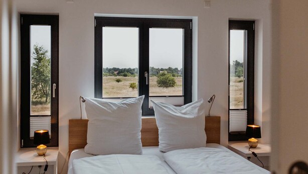 A bedroom with a large bed, two bedside tables with lamps, and a window offering a view of a field.