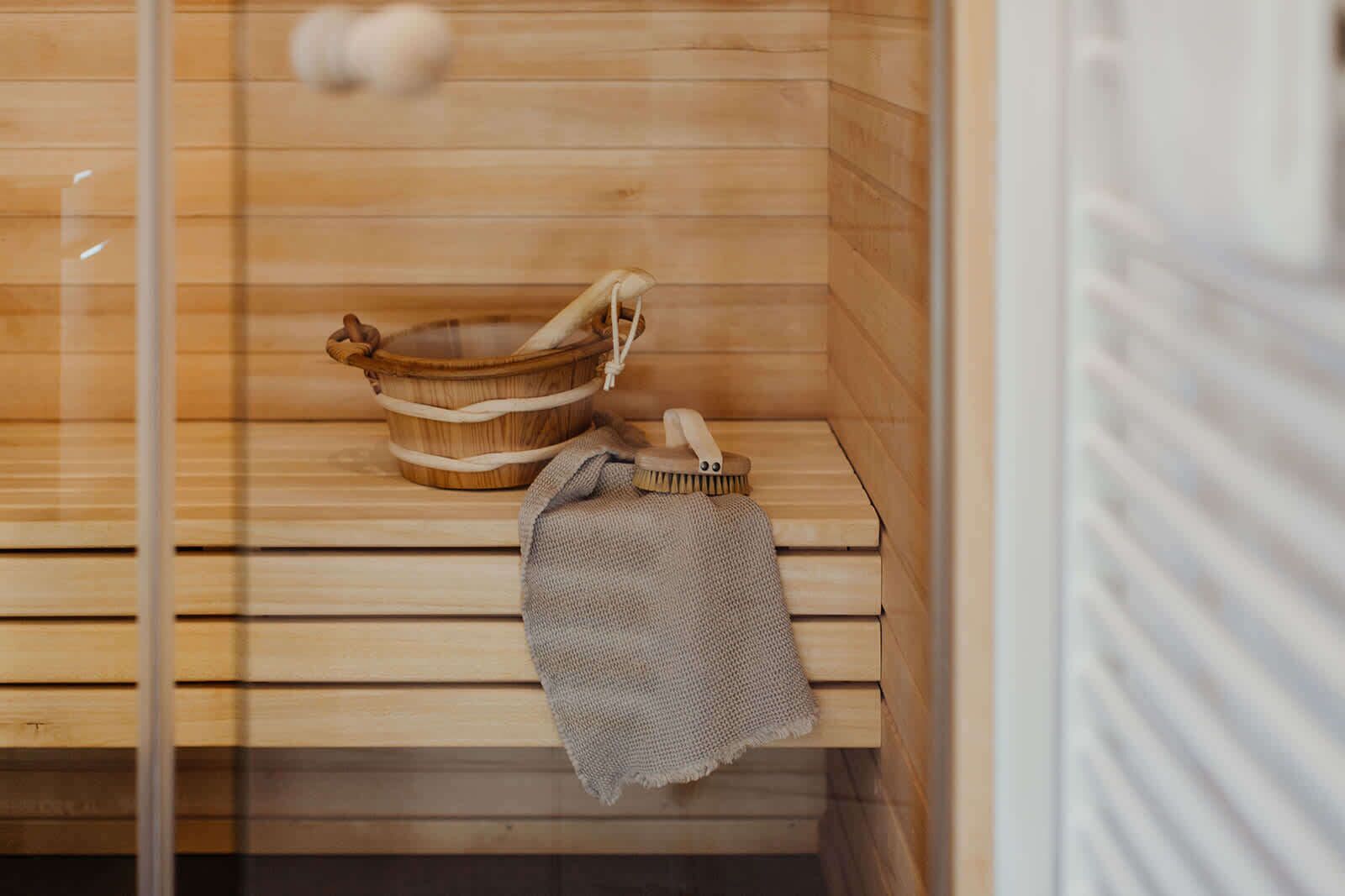 Eine Holzsauna mit einer Bank, einem Holzeimer und einem Handtuch.