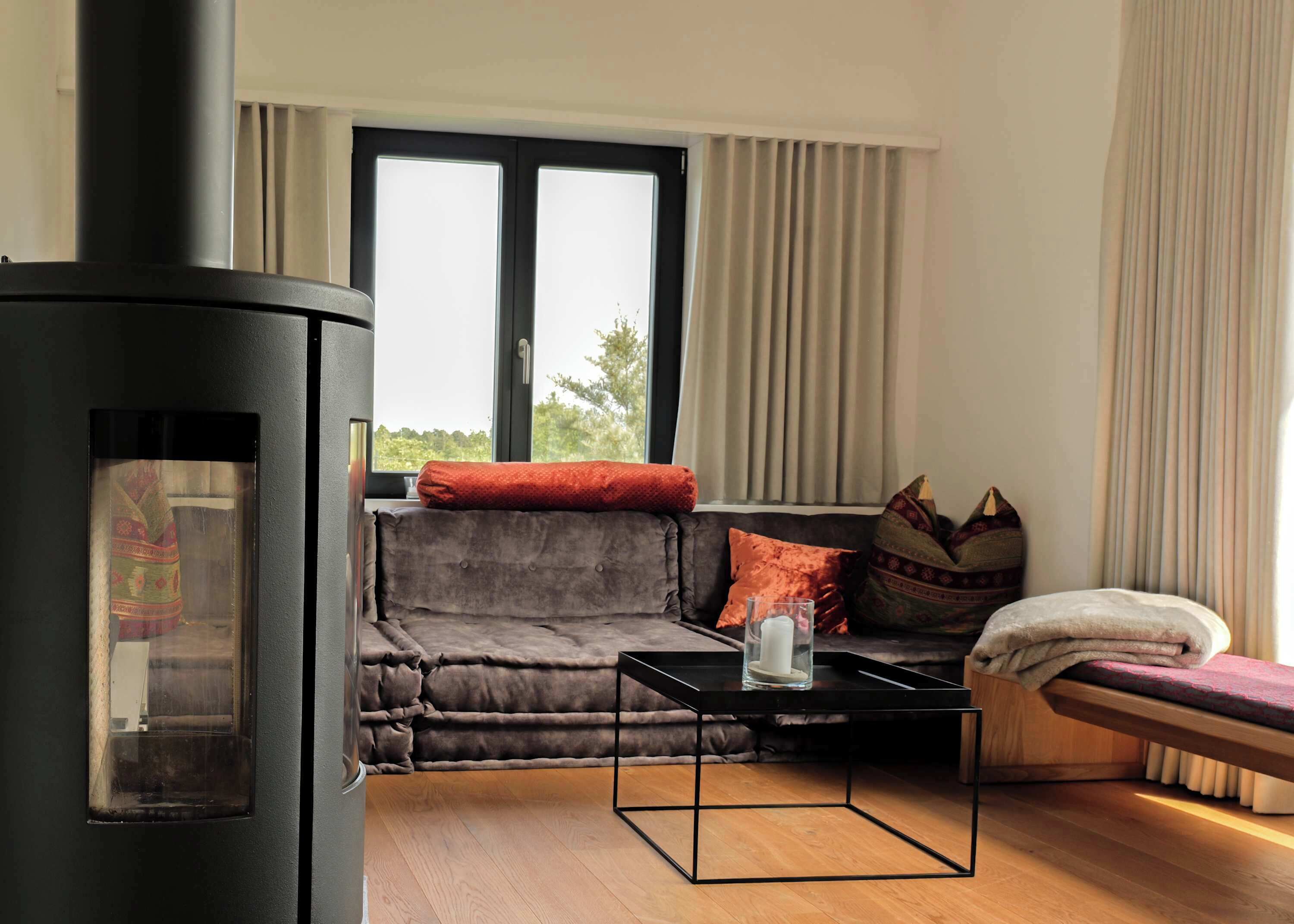 A cozy living room with a sofa, a small table, a bench, and a wood-burning stove.