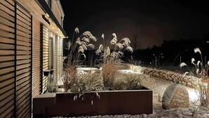 A modern building with a wooden exterior and a landscaped garden area featuring tall grasses and a stone wall.