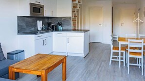 Ett modernt kök med vita skåp, en mikrovågsugn och en kaffebryggare. Det finns ett matbord i trä med vita stolar.