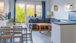 Ett modernt kök med en inbyggd mikrovågsugn, en matplats med trästolar och ett bord, en soffa och utsikt över grönområden utanför.