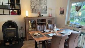 Ruokailutilassa on puinen pöytä, johon on katettu neljälle, takka ja ikkunasta avautuva näkymä vehreään maisemaan.