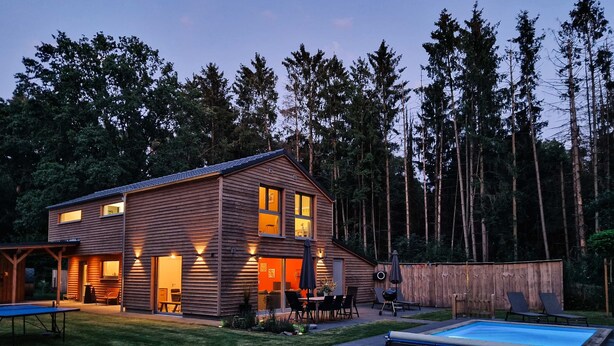 A two-story wooden house with a swimming pool, patio, and a deck.