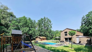 A backyard with a swing set, a small wooden shed, a pool, and a house with a covered patio.