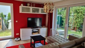 Ein modernes Wohnzimmer mit roter Wand, einem großen Flachbildfernseher, einem beigen Sofa, einem Couchtisch und einer Vitrine über dem Fernseher.