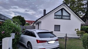 Ein weißer Audi A8 vor einem modernen weißen Haus mit Satteldach und großem Fenster.
