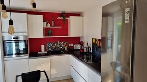 Eine kleine Küche mit weißen Schränken, einem Edelstahl-Kühlschrank, einer Mikrowelle und einem Spülbecken.