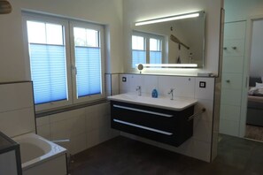 Un baño moderno con tocador blanco, un espejo grande y zona de ducha.