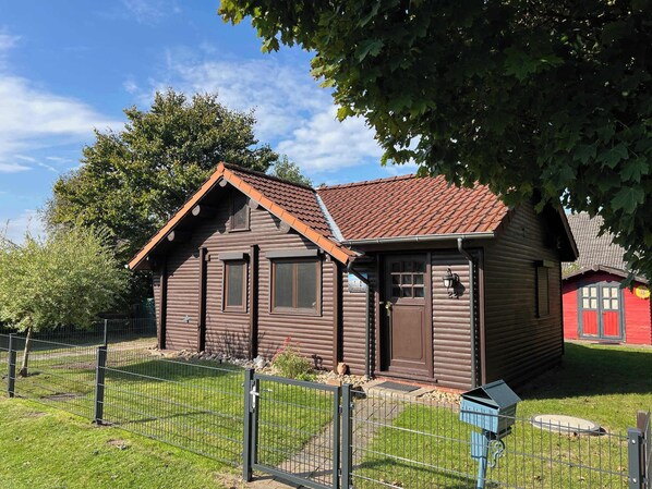 A wooden cabin with a tiled roof, a fenced yard, and a small porch.
