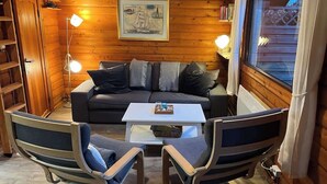 A cozy cabin interior with a sofa, two rocking chairs, a coffee table, and a framed picture on the wall.