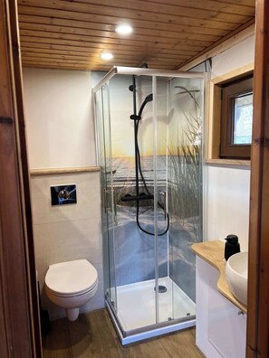A compact bathroom with a glass-enclosed shower, a toilet, and a sink.
