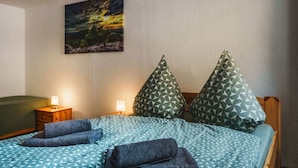 Una cama bien hecha con ropa de cama estampada y dos almohadas, una mesita de noche con lámpara, y un cuadro en la pared.