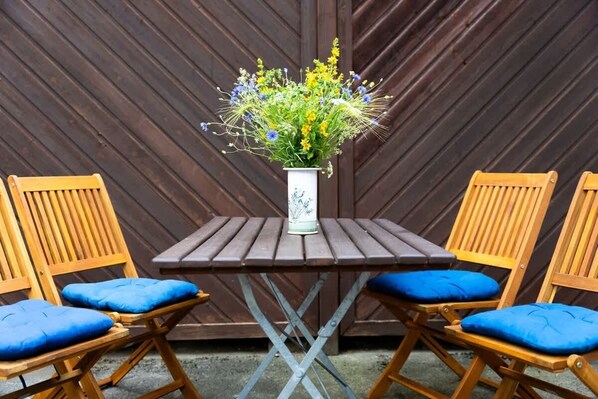 Una mesa de madera con un jarrón blanco lleno de flores, flanqueada por dos sillas de madera con cojines azules.