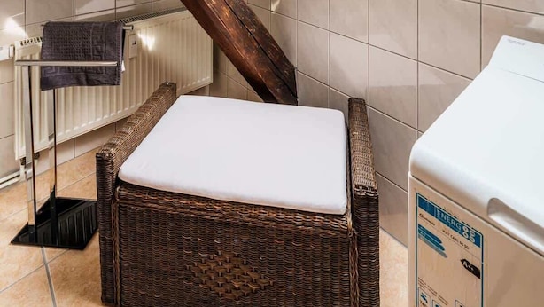 Un baño con tragaluz, una viga de madera, un banco de mimbre, un perchero y una lavadora.