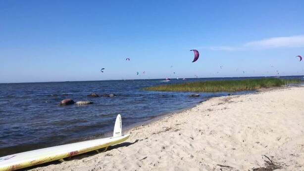 A beach with a surfboard, clear blue sky, and several kites flying.